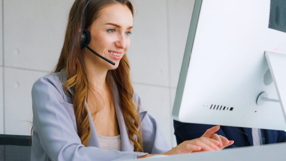Photo of a customer support agent wearing a headset and seated at a computer for telephone answering tips blog.