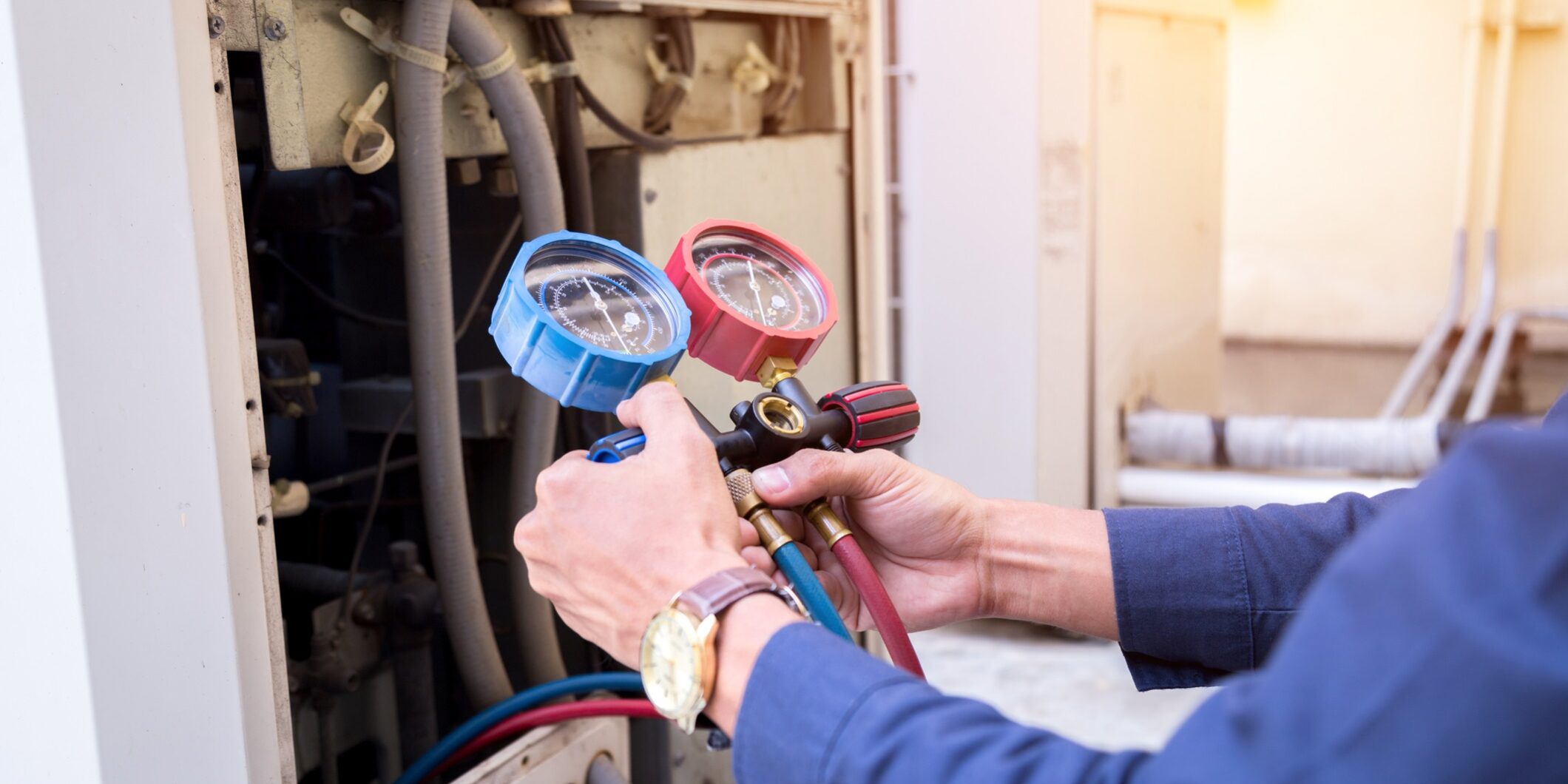 A technician checks an HVAC unit using red and blue gauges for HVAC and pest control calls blog.