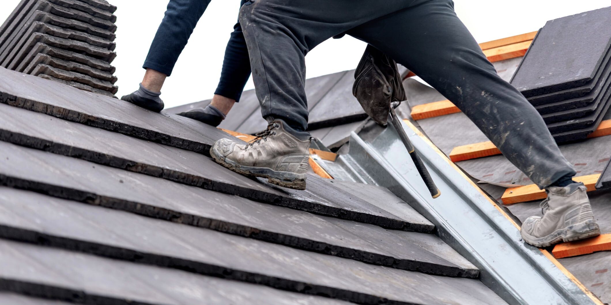 A roofer carefully places tiles on a sloped surface while standing on top of a building for why-your-roofing-company-needs-an-answering-service blog.
