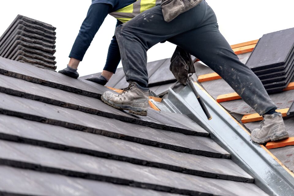 A roofer carefully places tiles on a sloped surface while standing on top of a building for why-your-roofing-company-needs-an-answering-service blog.