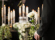 A man at a funeral home holds a white rose in front of an urn for your-funeral-home-needs-an-answering-service blog.