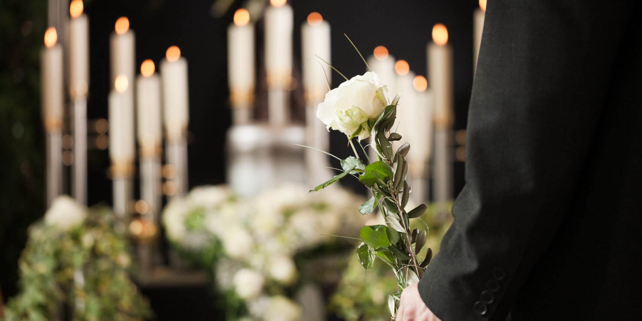 A man at a funeral home holds a white rose in front of an urn for your-funeral-home-needs-an-answering-service blog.