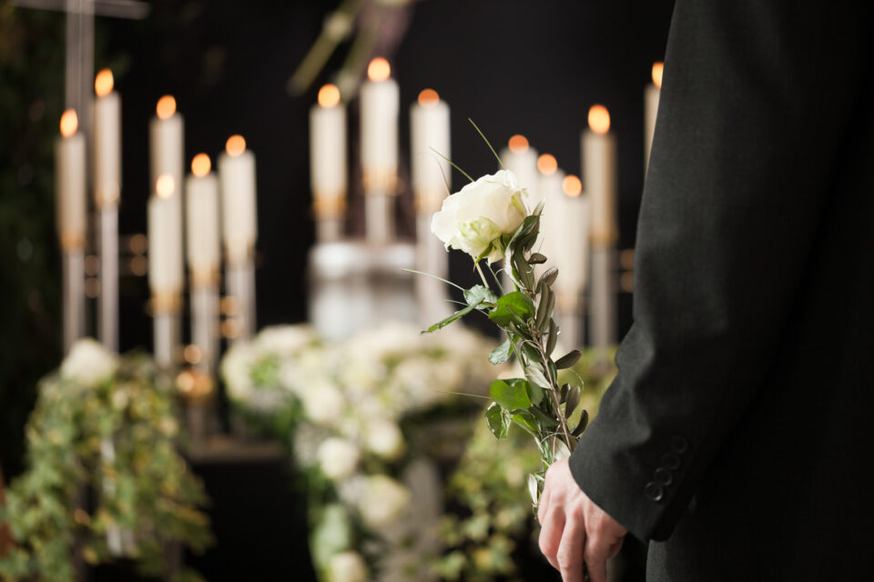 A man at a funeral home holds a white rose in front of an urn for your-funeral-home-needs-an-answering-service blog.